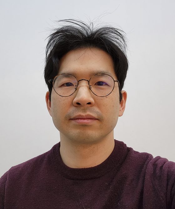정세훈. 밝은 회색 배경 앞, 와인색 스웨터